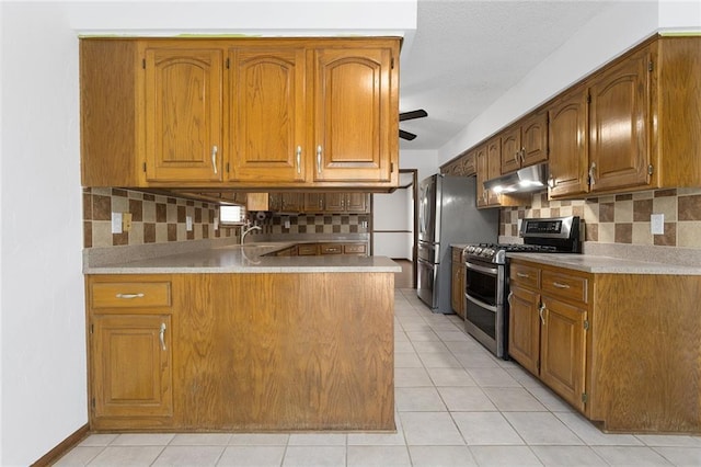 kitchen featuring under cabinet range hood, light tile patterned flooring, brown cabinetry, and range with two ovens