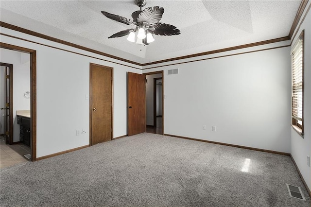 unfurnished bedroom with a textured ceiling, visible vents, a tray ceiling, ornamental molding, and light carpet