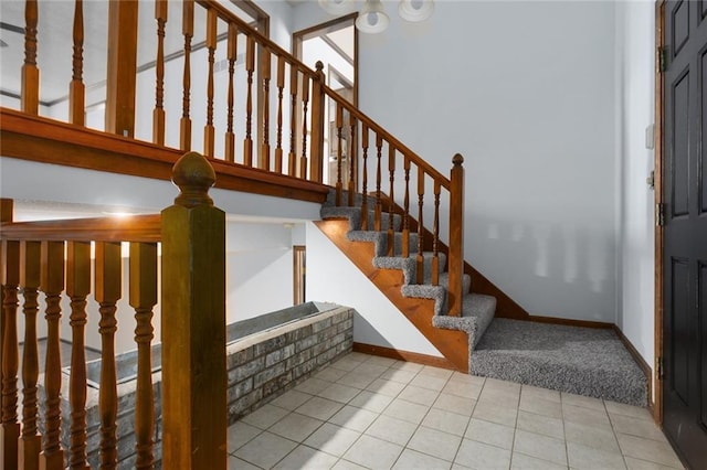 staircase with tile patterned floors, baseboards, and a towering ceiling