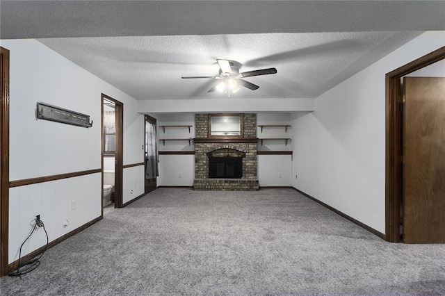 unfurnished living room featuring baseboards, ceiling fan, a textured ceiling, a brick fireplace, and carpet flooring