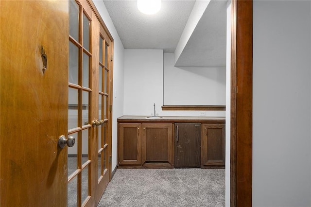 corridor featuring a sink, french doors, a textured ceiling, and carpet floors