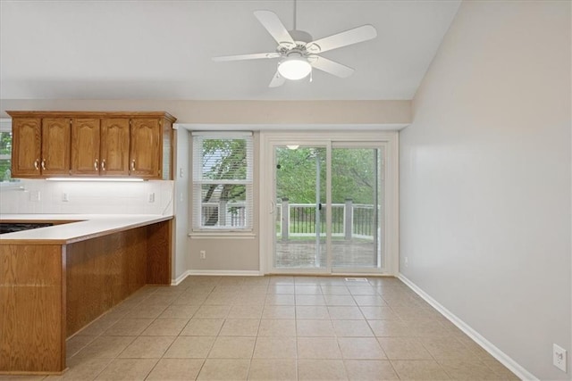 kitchen featuring light countertops, brown cabinetry, baseboards, decorative backsplash, and vaulted ceiling