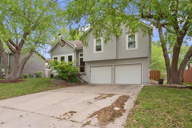 tri-level home with concrete driveway, fence, a front lawn, and a garage