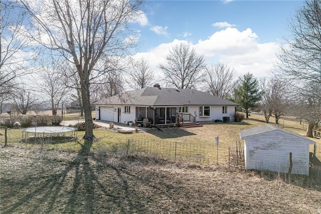 back of house featuring a trampoline, a fenced front yard, a lawn, a chimney, and a garage