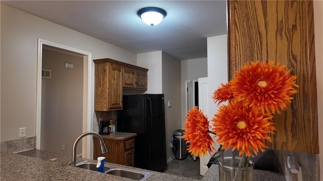 kitchen featuring visible vents, a textured ceiling, freestanding refrigerator, and a sink