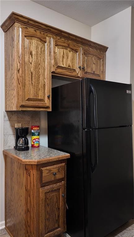 kitchen with decorative backsplash, a textured ceiling, brown cabinetry, and freestanding refrigerator