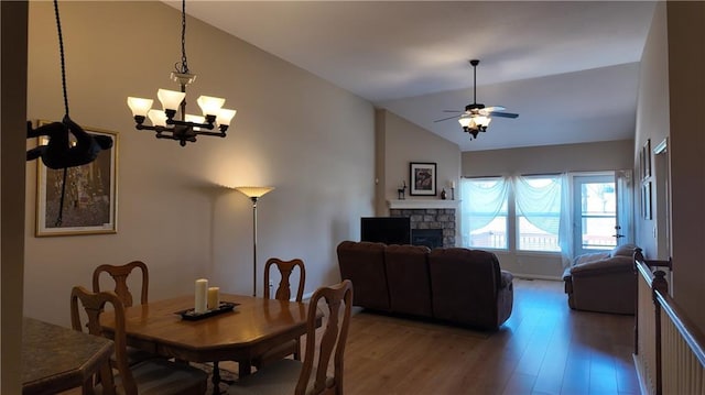 dining room with a fireplace, vaulted ceiling, ceiling fan with notable chandelier, and light wood-style floors