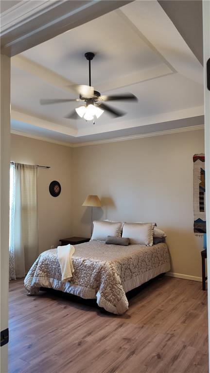 bedroom featuring a tray ceiling, wood finished floors, baseboards, and ceiling fan