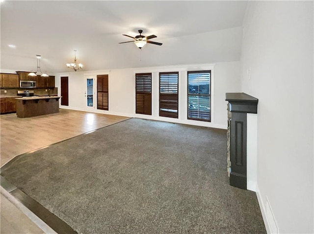 unfurnished living room with light wood-style flooring, ceiling fan with notable chandelier, baseboards, and light carpet