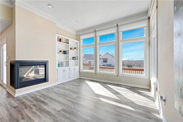 unfurnished living room featuring built in shelves, baseboards, a multi sided fireplace, ornamental molding, and wood finished floors