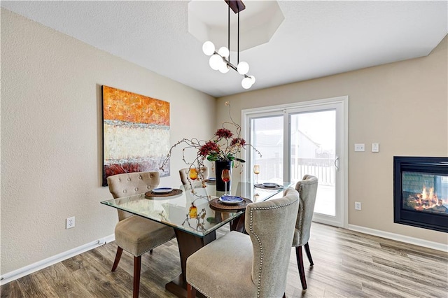 dining area with a multi sided fireplace, baseboards, wood finished floors, and a chandelier