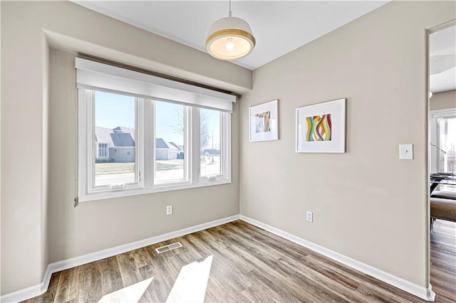 spare room featuring plenty of natural light, visible vents, baseboards, and wood finished floors