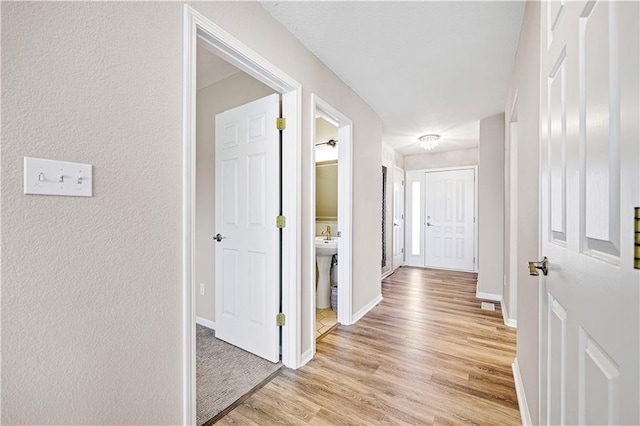 hallway featuring baseboards, light wood-style floors, and a textured wall