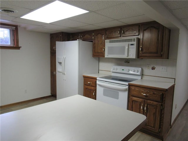 kitchen with tasteful backsplash, a drop ceiling, white appliances, and light countertops