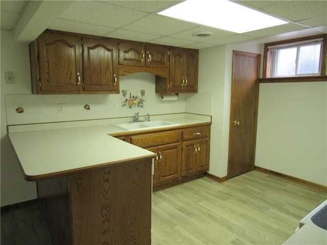 kitchen featuring a peninsula, light wood-style flooring, a sink, light countertops, and a paneled ceiling