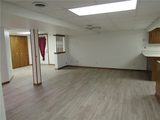 finished below grade area with visible vents, light wood-type flooring, a drop ceiling, and baseboards