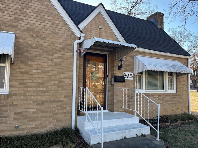 view of exterior entry featuring brick siding and a chimney