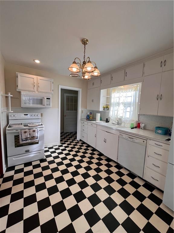 kitchen with light floors, light countertops, a notable chandelier, white cabinets, and white appliances