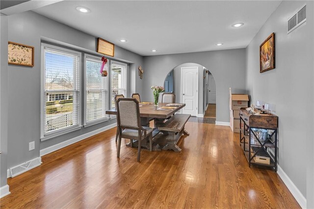 dining area with wood finished floors, visible vents, arched walkways, and baseboards