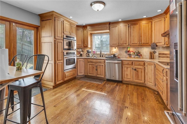 kitchen featuring light wood finished floors, stainless steel appliances, light countertops, under cabinet range hood, and tasteful backsplash