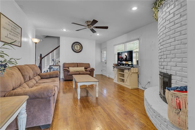 living area with a brick fireplace, ceiling fan, stairs, recessed lighting, and light wood-style floors