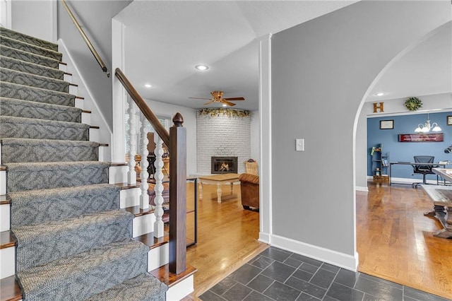 staircase featuring wood finished floors, a ceiling fan, baseboards, a fireplace, and arched walkways