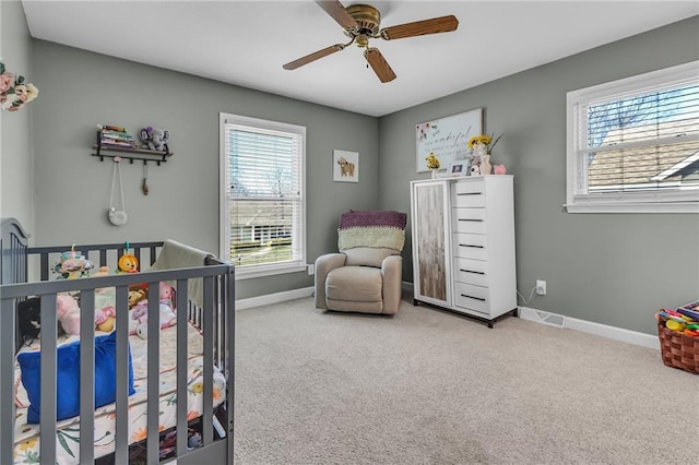 bedroom featuring a crib, carpet, baseboards, and a ceiling fan