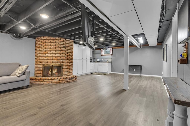 below grade area with a brick fireplace, baseboards, and light wood finished floors