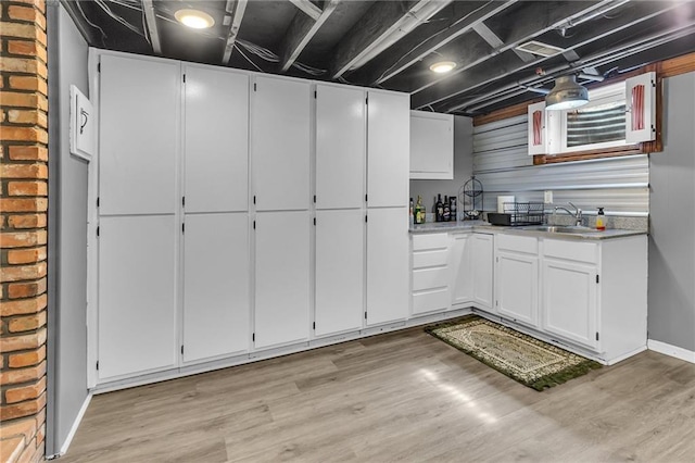 kitchen with baseboards, light wood-type flooring, light countertops, white cabinets, and a sink