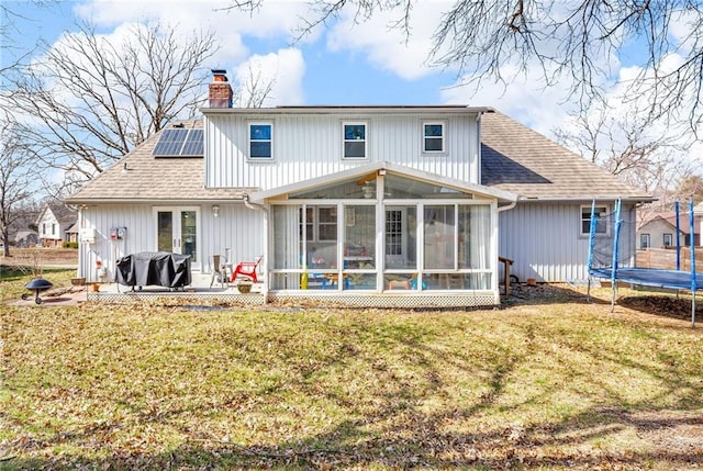 back of house featuring solar panels, a sunroom, a chimney, a trampoline, and a lawn