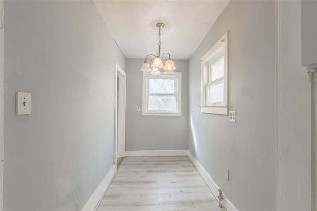 unfurnished dining area with an inviting chandelier, baseboards, and light wood finished floors