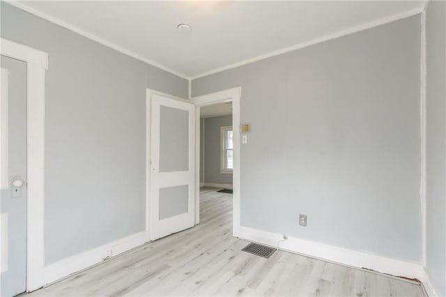 empty room with visible vents, wood finished floors, baseboards, and ornamental molding