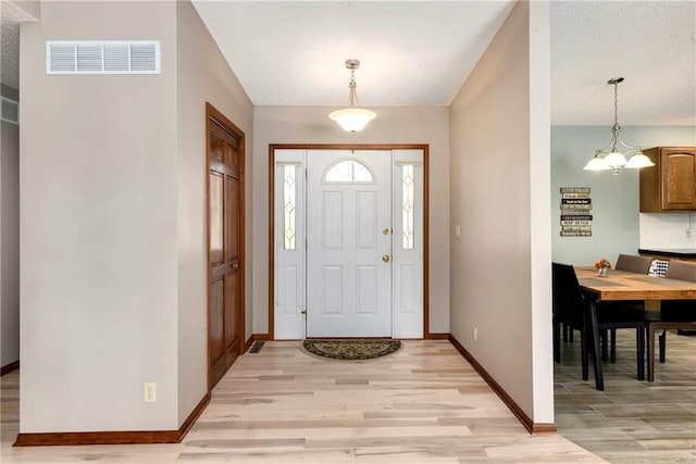 entryway featuring a notable chandelier, baseboards, visible vents, and light wood finished floors