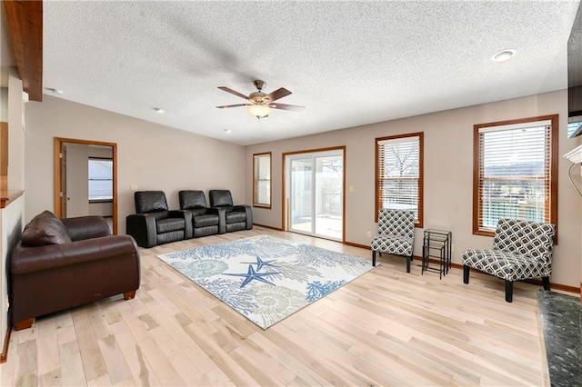 living area with light wood-type flooring, baseboards, a textured ceiling, and a ceiling fan