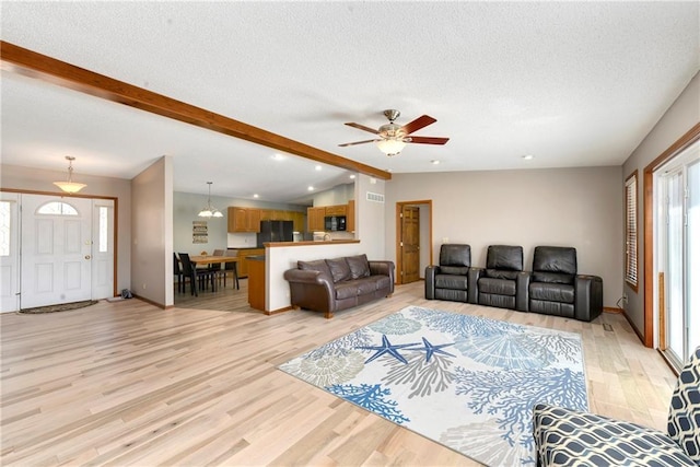 living area featuring lofted ceiling with beams, light wood-type flooring, and a textured ceiling