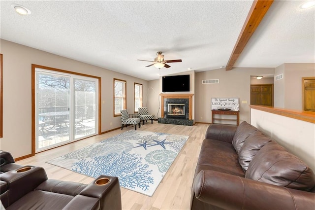 living room with light wood finished floors, visible vents, a high end fireplace, and a textured ceiling