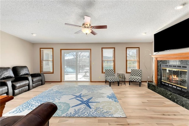 living area with a ceiling fan, baseboards, light wood-style flooring, a fireplace, and a textured ceiling