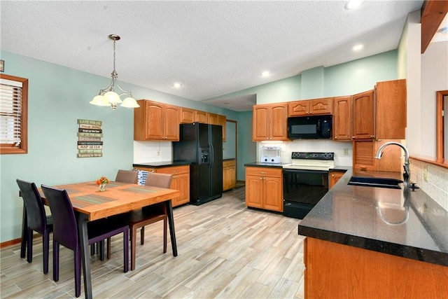 kitchen featuring lofted ceiling, a sink, black appliances, dark countertops, and light wood-type flooring