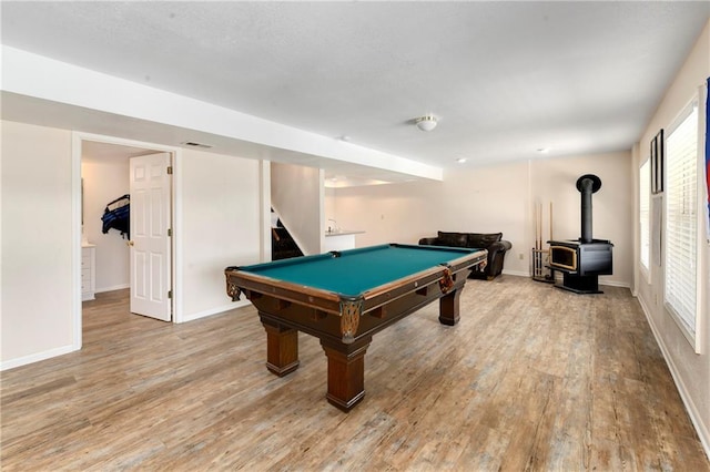 recreation room featuring a wood stove, visible vents, light wood-type flooring, and baseboards