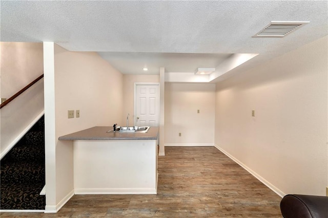 kitchen featuring visible vents, baseboards, a peninsula, wood finished floors, and a sink