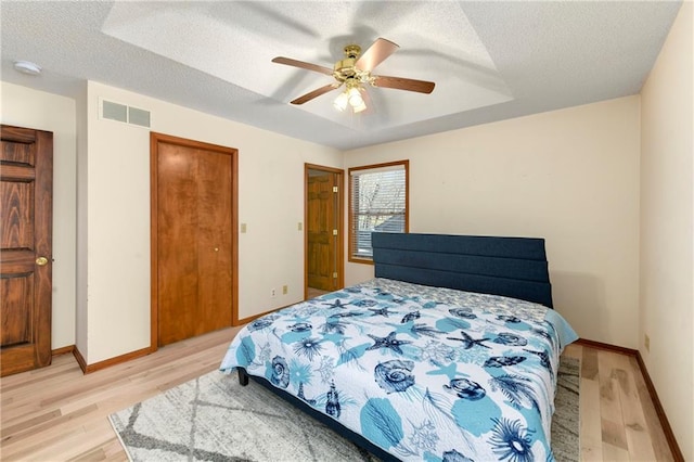 bedroom with visible vents, baseboards, a textured ceiling, and light wood-style flooring