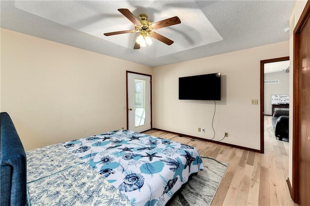 bedroom with baseboards, a tray ceiling, light wood-style floors, a textured ceiling, and a ceiling fan