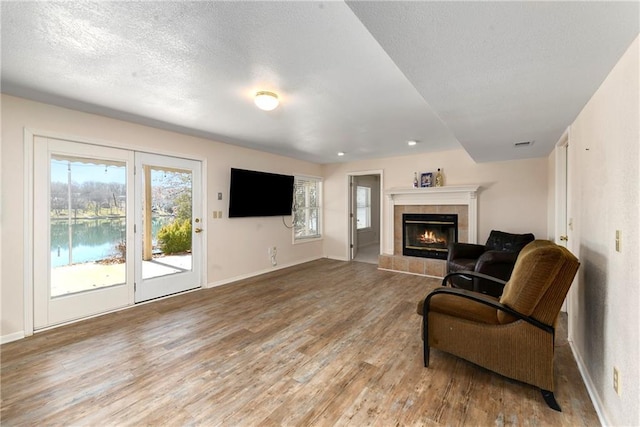 living room featuring visible vents, baseboards, a fireplace, light wood-style floors, and a textured ceiling