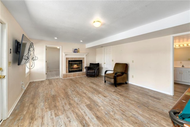 sitting room with light wood-type flooring, baseboards, a textured ceiling, and a tiled fireplace