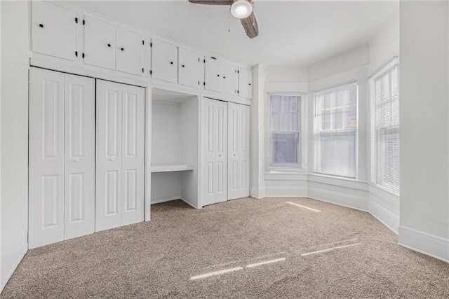 unfurnished bedroom with carpet flooring, two closets, and a ceiling fan