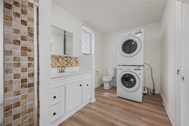 clothes washing area featuring baseboards, laundry area, a sink, stacked washer / drying machine, and light wood-type flooring