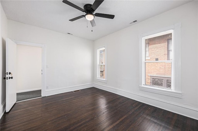 empty room with visible vents, plenty of natural light, and dark wood-type flooring