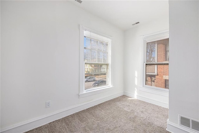 carpeted empty room featuring a wealth of natural light, visible vents, and baseboards