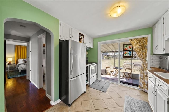 kitchen with electric range, arched walkways, white cabinetry, and freestanding refrigerator