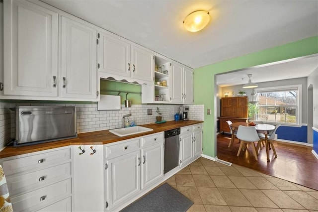 kitchen with a sink, wooden counters, stainless steel dishwasher, and white cabinetry